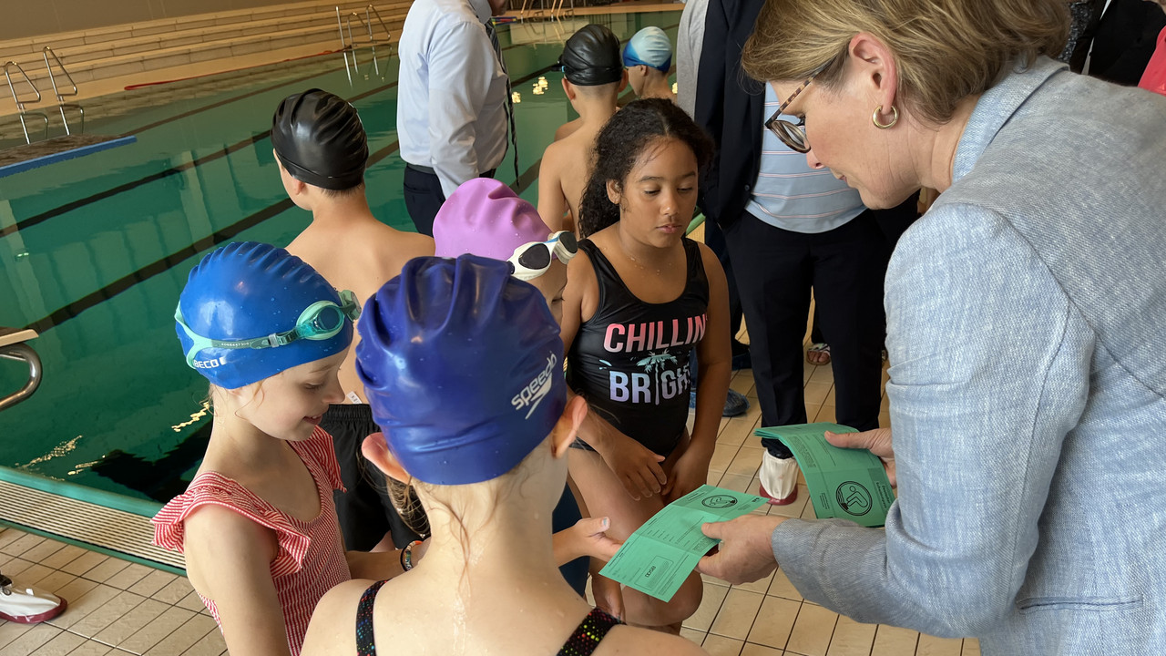 Zu sehen ist Bildungsministerin Dr. Stefanie Hubig, die die ersten Schwimmabzeichen an die Schülerinnen und Schüler der Grundschule am Mühlbach in Saulheim übergibt.