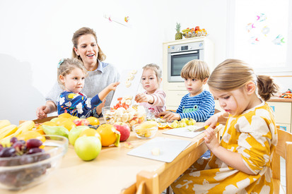 Kinder helfen einer Fachkraft bei der Zubereitung eines Obstsalats.