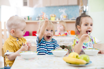 Drei Kinder sitzen an einem Tisch und essen.