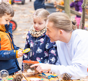 Kindern sind mit Erzieher draußen und betrachten Tannenzapfen mit Hilfe eine Lupe.