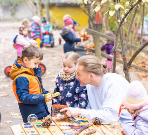 Kindern sind mit Erzieher draußen und betrachten Tannenzapfen mit Hilfe eine Lupe.