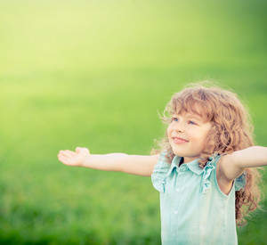 Ein Mädchen steht mit ausgebreiteten Armen lächelnd auf einer Wiese.
