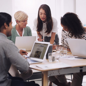 Mitarbeitende sitzen um einen Tisch, zum Teil an Laptops, und arbeiten gemeinsam