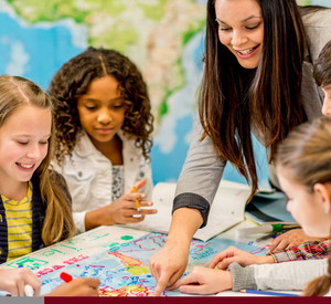 Vier Kinder arbeiten gemeinsam an einem Gruppenprojekt. Eine Lehrkraft betreut die Kinder. 