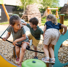 Drei Kinder klettern auf einem Spielplatz auf einem Klettergerüst.