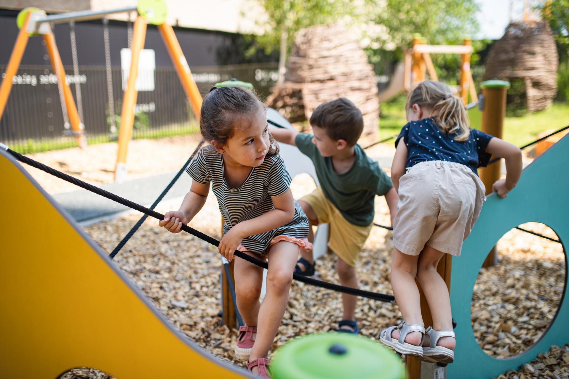 Drei Kinder klettern auf einem Spielplatz auf einem Klettergerüst.