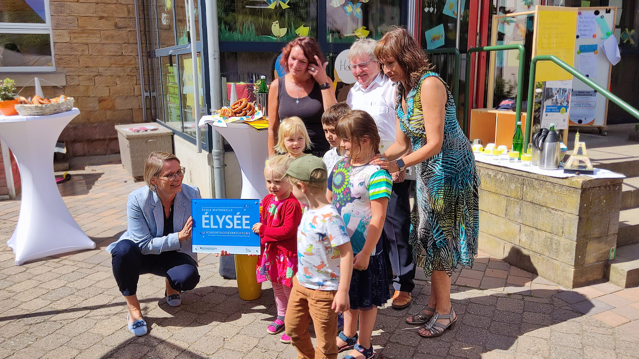 Bildungsministerin Dr. Stefanie Hubig (links) überreicht die Elysée-Plakette an die Kinder der Kita Vogelnest in Deidesheim und ihre Leiterin Ulrike Stepic (Zweite von links).