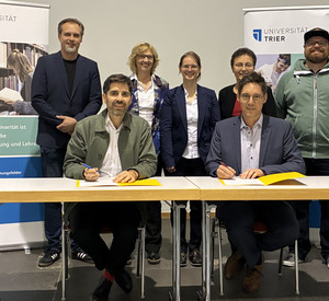 Bildungsminister Sven Teuber (vorne links) und der Vizepräsident der Universität Trier, Prof. Dr. Matthias Busch, unterzeichnen die Kooperationsvereinbarung zum Weiterbildungslehrgang für das Pflichtfach Informatik.