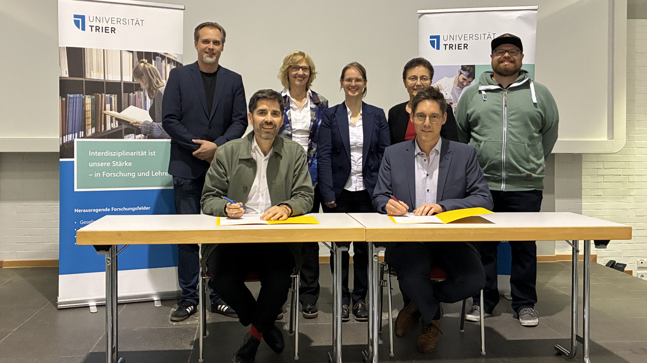 Bildungsminister Sven Teuber (vorne links) und der Vizepräsident der Universität Trier, Prof. Dr. Matthias Busch, unterzeichnen die Kooperationsvereinbarung zum Weiterbildungslehrgang für das Pflichtfach Informatik.