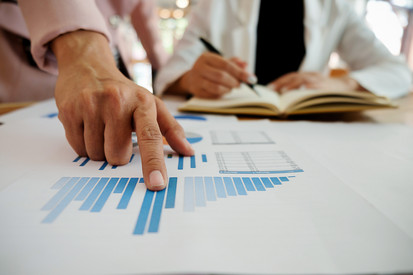 Ein Blatt mit einem Säulendiagramm liegt auf einem Tisch. Eine Hand zeigt darauf.