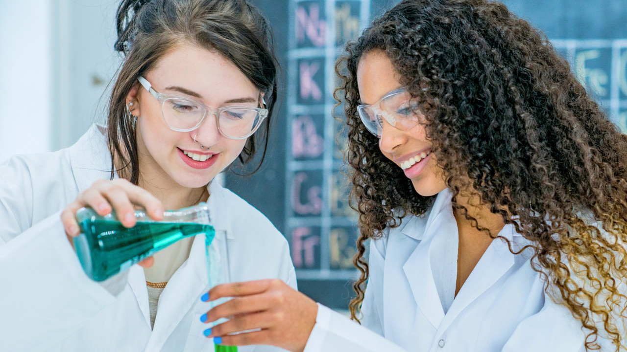 Junge Frauen experimentieren in Laborkitteln.