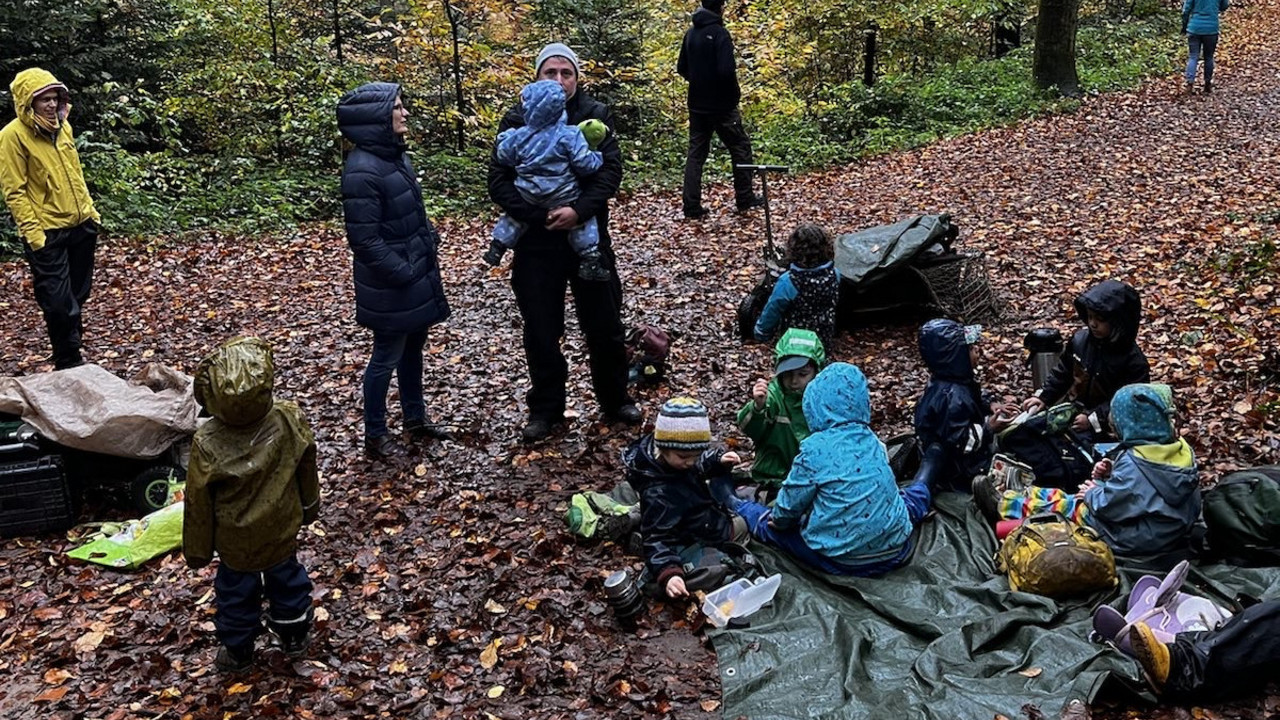 Auf dem Foto sieht man Erzieherinnen und Erzieher mit Kindern im Wald.