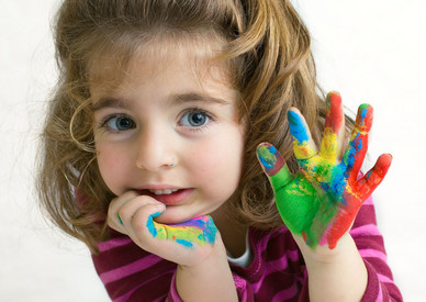 Mädchen hält eine mit Farbe bunt beschmierte Hand in die Luft.